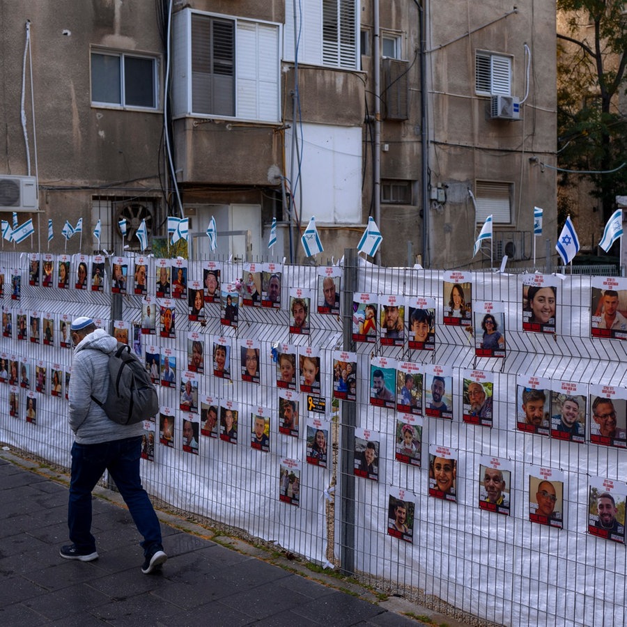 Ein Mann geht an einem Zaun mit Fotos von Geiseln vorbei, meist israelische Zivilisten, die während des Hamas-Angriffs auf Israel am 7. Oktober entführt wurden. © picture alliance/dpa/AP Foto: Oded Balilty