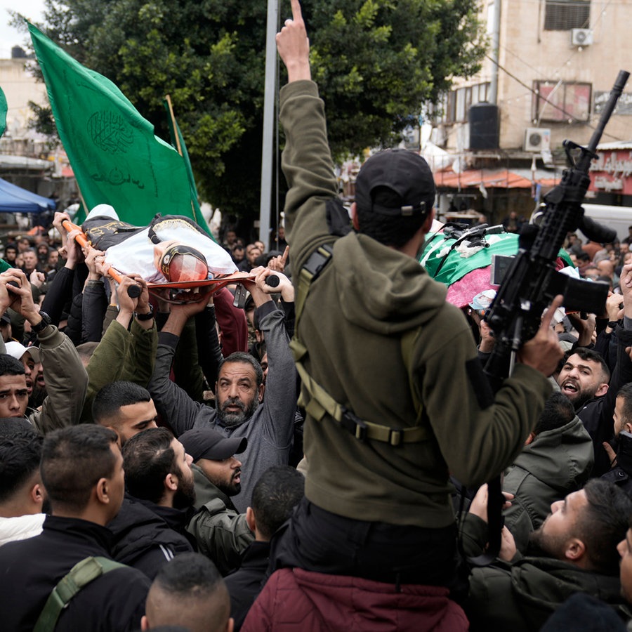 Palästinensische Bewaffnete marschieren mit den Leichen von Kämpfern, die in die Fahnen des palästinensischen Islamischen Dschihad gehüllt sind und bei einer israelischen Militäraktion im Ibn-Sina-Krankenhaus getötet wurden. © AP Foto: Majdi Mohammed