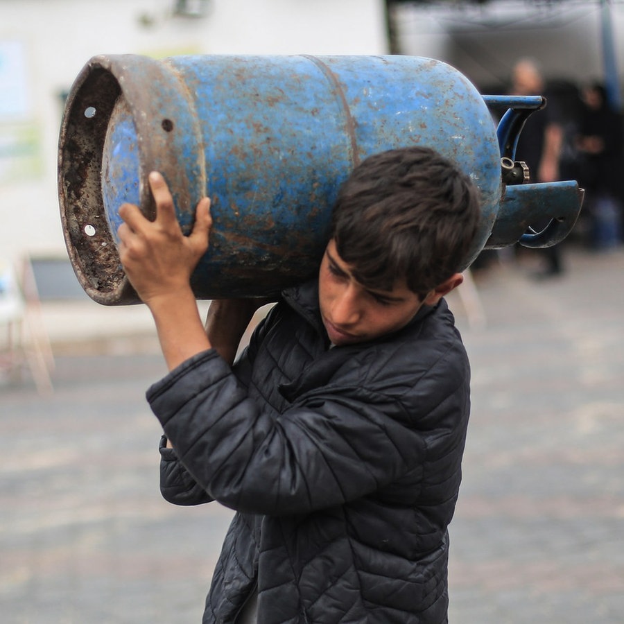 Ein Palästinenser trägt seine Flüssiggasflasche, nachdem er sie am zweiten Tag der viertägigen Feuerpause zwischen Israel und der Terrororganisation Hamas wieder aufgefüllt hat. © picture alliance/dpa | Foto: Mohammed Talaten