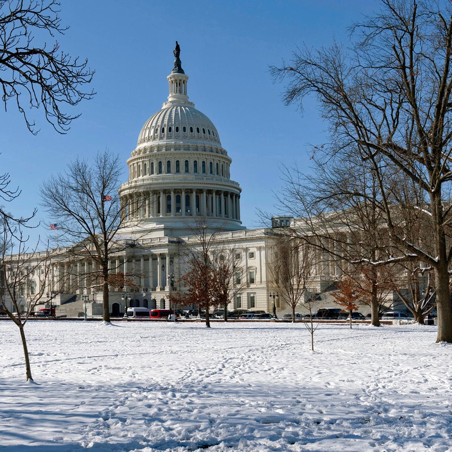 Das US-Kapitol in Washington (USA) ist an einem sonnigen Wintertag hinter eine mit Schnee bedeckten Wiese zu sehen. © AP/dpa Foto: Jose Luis Magana