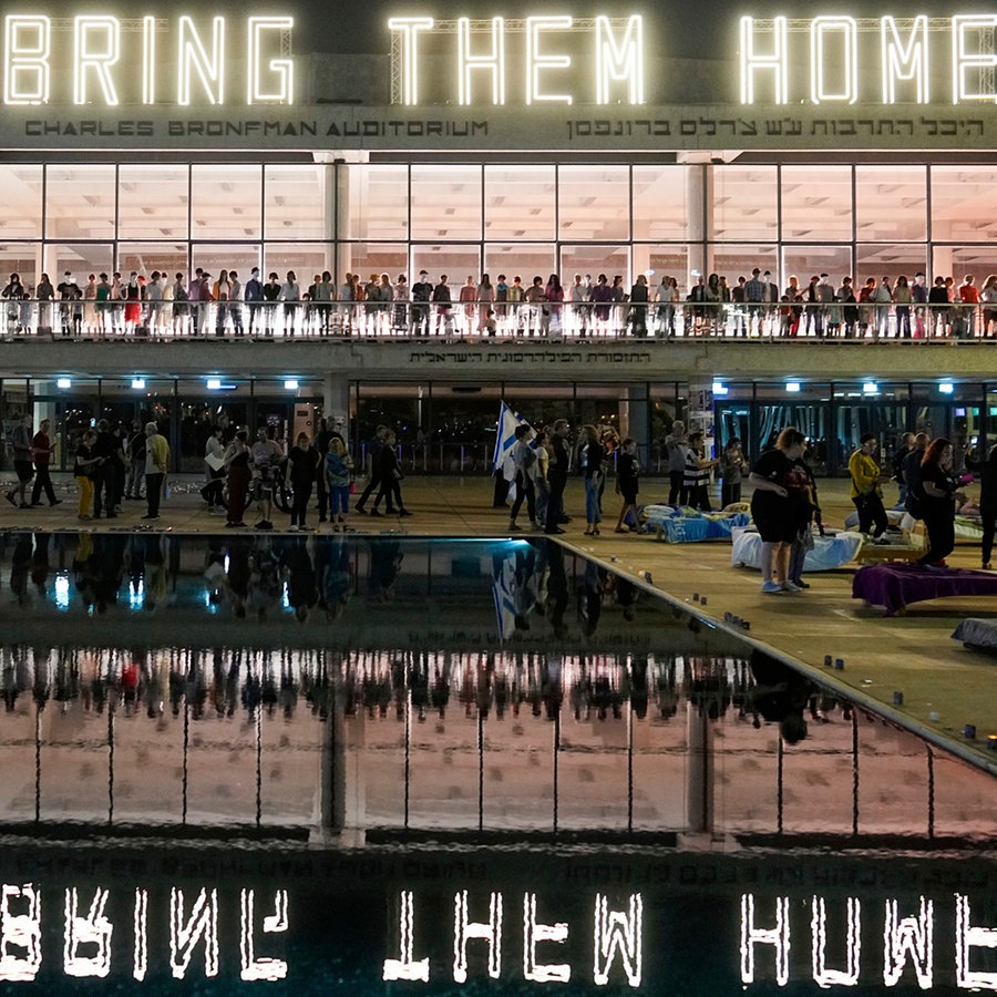 Menschen stehen unter einer Leuchtschrift mit dem Text "Bring Them Home" (Bringt sie nach Hause), bei einer Demonstration, die die Rückkehr der Geiseln fordert, die bei dem Hamas-Angriff vom 07.10.2023 in Israel entführt wurden. © AP/dpa Foto: Ohad Zwigenberg