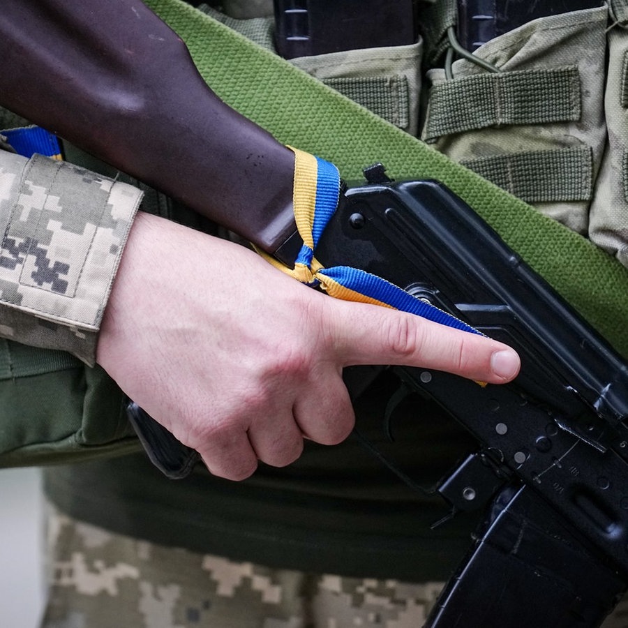 Ein ukrainischer Soldat hält ein Gewehr in der Hand, an das ein Band in den ukrainischen Farben gebunden ist. © picture alliance/dpa Foto: Kay Nietfeld