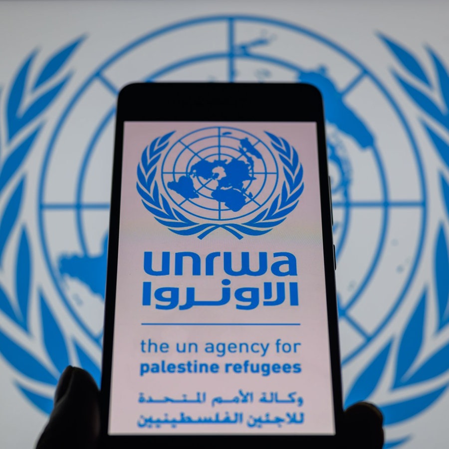 Das Logo des UNRWA, des Hilfswerd der Vereinten Nationen für Palästina-Flüchtlinge, ist auf einem Smarphone-Bildschirm zu sehen, im Hintergrund erkennt man das Logo der Vereinten Nationen. © picture alliance / NurPhoto Foto: Jonathan Raa