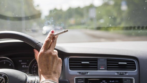 Eine Frau sitzt im Auto in hält eine Zigarette in die Luft. © imago Foto: imago/imagebroker