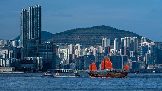 Ein Boot mit roten Segeln vor der Skyline von Hongkong © picture alliance / Nur Photo Foto: Marc Fernandes