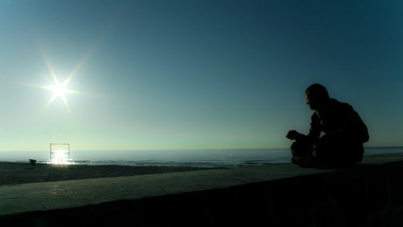 Eine Person sitzt auf einer Mauer und blickt aufs Meer. © Bengelsdorf/photocase.de Foto: Bengelsdorf