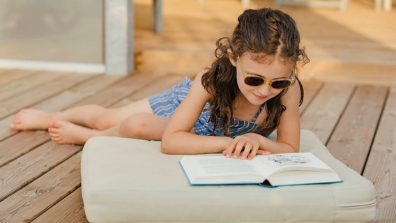 Ein junges Mädchen liegt auf dem Bodenund liest ein Buch © IMAGO/ imagebroker 