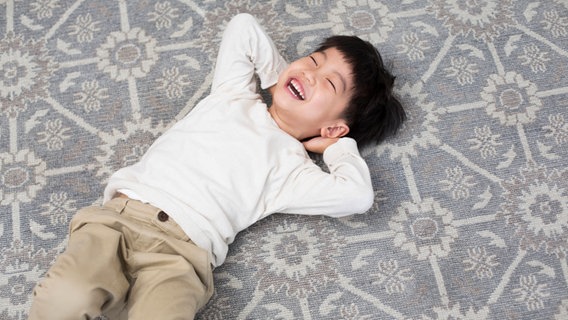Ein Kind liegt auf dem Boden und lacht © IMAGO / Blue Jean Images 