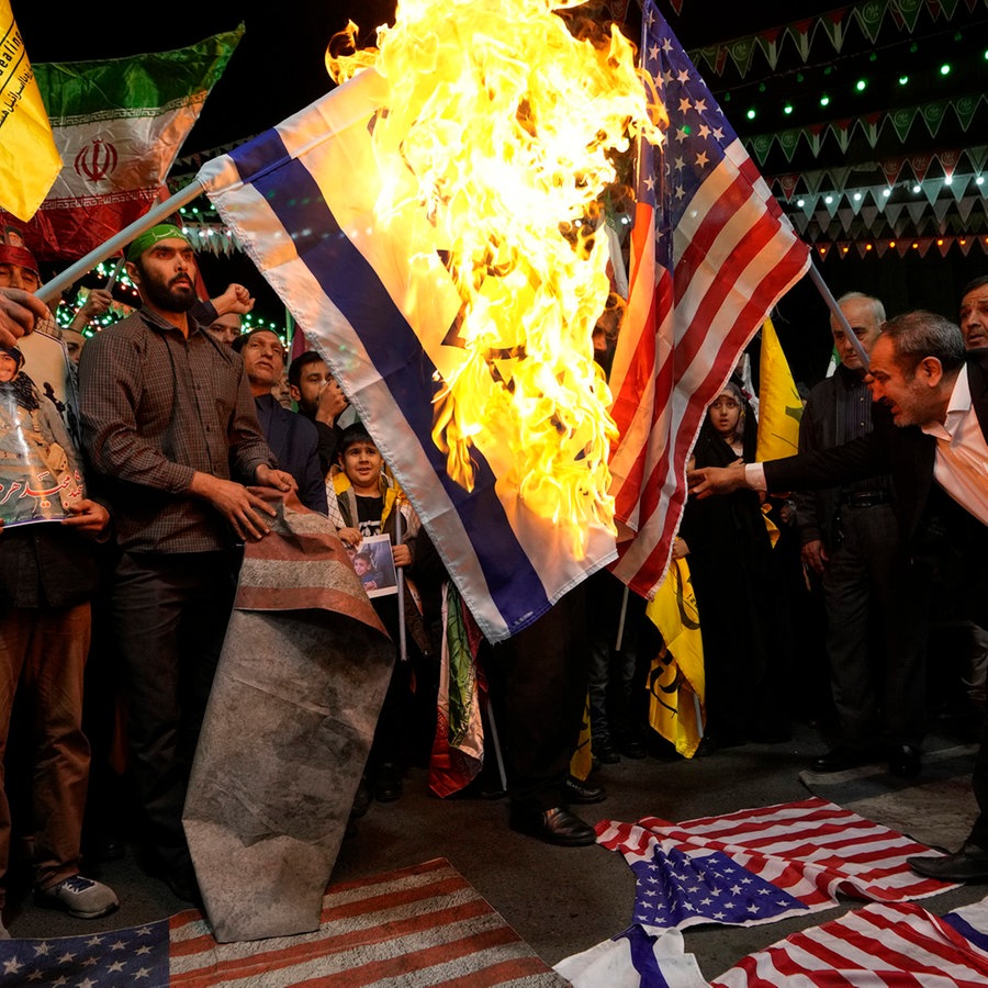 Iranische Demonstranten verbrennen US-amerikanische und israelische Fahnen, um die Tötung von Mitgliedern der iranischen Revolutionsgarden zu verurteilen. © Vahid Salemi/AP/dpa 