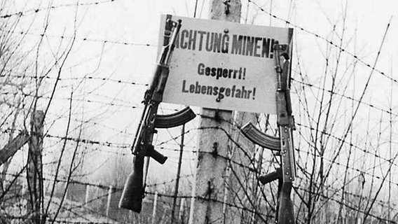 An einem Grenzübergang sind ein Minenwarnschild, sowie zwei Maschinengewehre befestigt. © NDR Foto: Hermann Pröhl