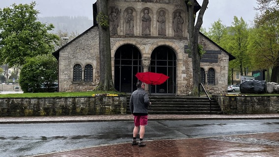 Ein Mann steht mit einem roten Regenschirm vor einer Kirche in Goslar. © NDR Foto: Falk Schwarz