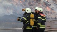 Three firefighters stand in front of a pile of burning compost. © NDR Photo: Stefan Rampfel