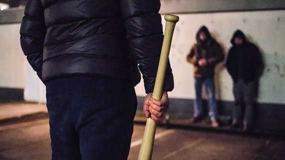 Eine Person steht mit einem Baseballschläger in der Hand auf einer Straße. © NDR Foto: Julius Matuschik