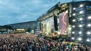 Many people stand in front of a big stage, in the background, we see a giant wheel. © Messe Hannover Photo: Rainer Jensen