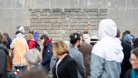Besucher stehen nach einer Gedenkveranstaltung zum 79. Jahrestag der Befreiung des ehemaligen Konzentrationslagers Bergen-Belsen vor einer Inschriftenwand auf dem Gelände der Gedenkstätte. © Michael Matthey/dpa Foto: Michael Matthey/dpa