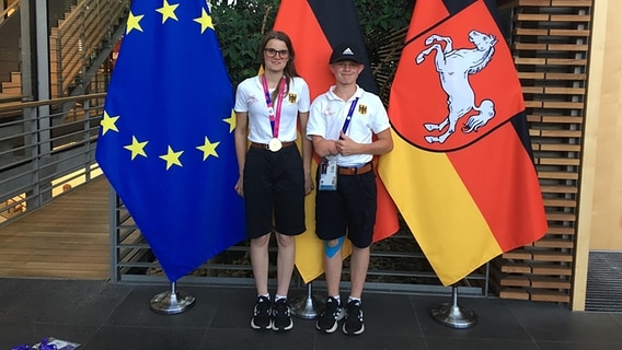 Zwei Olympioniken stehen mit Medaillen vor Fahnen. © Beate Meineke Foto: Beate Meineke
