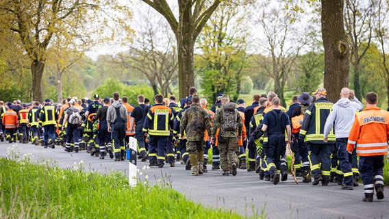 Einsatzkräfte der Feuerwehr und Soldaten der Bundeswehr gehen bei der Suche nach einem vermissten Jungen aus Bremervörde auf einer Straße im Landkreis Stade entlang. © dpa Foto: Moritz Frankenberg