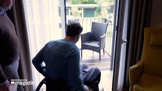 Ein Mann in einem Rollstuhl fährt auf einen Balkon eines Hotelzimmers © NDR Foto: NDR Screenshot