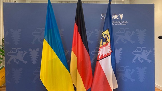 Die Flaggen der Ukraine, Deutschlands und von Schleswig-Holstein stehen nebeneinander vor einer Wand. © Anna-Katharina Stratmann Foto: Anna-Katharina Stratmann