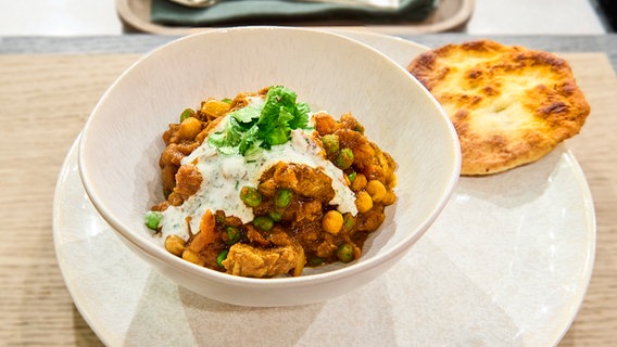 Lamm-Kichererbsen-Curry mit Garlic Naan auf einem Teller angerichtet. © NDR / Die Fernsehmacher Foto: Gunnar Nicolaus