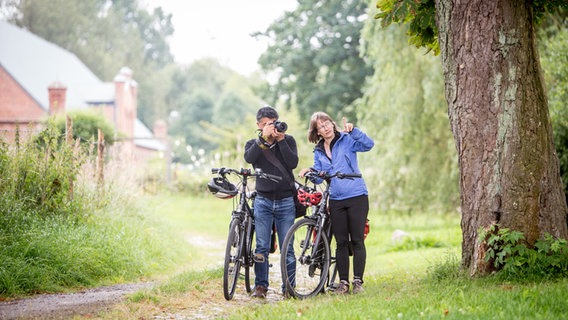 Zwei Radfahrer stehen auf einem Weg vor dem Schloss Ludwigsburg in Vorpommern, der eine macht ein Foto. © TMV/Krauss 
