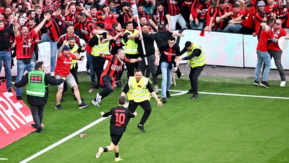 Leverkusens Florian Wirtz bejubelt einen Treffer und versucht die Fans zu beruhigen und von einem verfrühten Platzsturm abzuhalten. © picture alliance/dpa | David Inderlied 