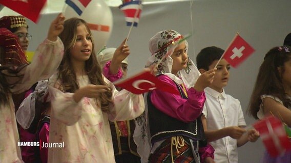 Kinder auf einer Bühne schwenken die Nationalflaggen verschiedener Länder. © Screenshot 