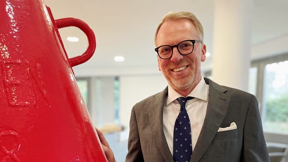 Der Leiter der Generaldirektion Wasserstraßen und Schifffahrt Eric Oehlmann im Portrait. Hinter ihm: ein Hafen. © Wasserstraßen- und Schifffahrtsverwaltung des Bundes (WSV) Foto: Wasserstraßen- und Schifffahrtsverwaltung des Bundes (WSV)