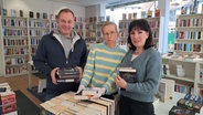 Ein Mann ( Ladenbetreiber Hermann Florkowski )  und ehrenamtliche Verkäuferinnen stehen nebeneinander im Ladengeschäft von "Aktion Buch" in Farmsen. Hinter ihnen prall gefüllte Bücherregale. © NDR Foto: Petra Volquardsen