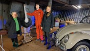 Unter Deck eines großen Schiffes stehen zwei Frauen und ein Mann vor eine Vogel Strauss Figur. Es sind Leute von der  Crew der CapSan Diego: Gesa Rädecker, Matrose Sören, Geschäftsführerin Ann-Kathrin Ruess. Neben ihnen sieht man einen Teil von einem VW Käfer. © NDR / Petra Volquardsen Foto: Petra Volquardsen