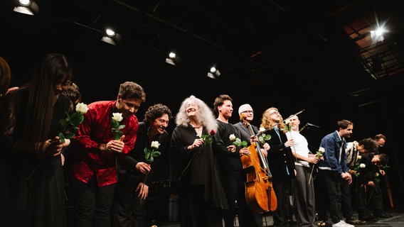 Auf der Bühne verbeugt sich eine Reihe von Musikern und Musikerinnen mit weißen Rosen in der Hand. In der Mitte die Pianistin Martha Argerich. © Daniel Dittus Foto: Daniel Dittus