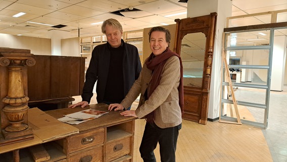 Neben einem alten Verkaufstresen stehen zwei Männer vom Stadtmuseum Harburg ( Jens Brauer und Rainer Maria Weiss). © NDR Foto: Petra Volquardsen