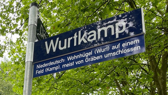 Ein Straßenschild mit der Aufschrift "Wurtkamp". Darunter: ein weiteres Schild, das den plattdeutschen Namen erklärt. © NDR - Gerrit Hoss Foto: NDR - Gerrit Hoss