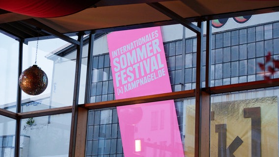 Eine rosanes Banner an einer Industriewand. Auf dem Banner steht "Internationales Sommerfestival Kampnagel". © Kampnagel / Fabian Hammerl Foto: Fabian Hammerl