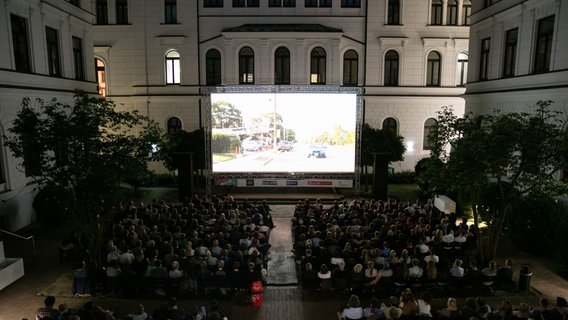 Eine Kinoleinwand im Innenhof eines Rathauses. Viele Besucher auf Stühlen. Auf der Leinwand wird ein Film gezeigt. Es ist bereits dunkel. © Jan Brandes Foto: Jan Brandes