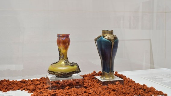 Auf rotem Sand stehen zwei bunte Zinnvasen in einer Vitrine im Museum © Museum für Kunst und Gewerbe Foto: Henning Rogge