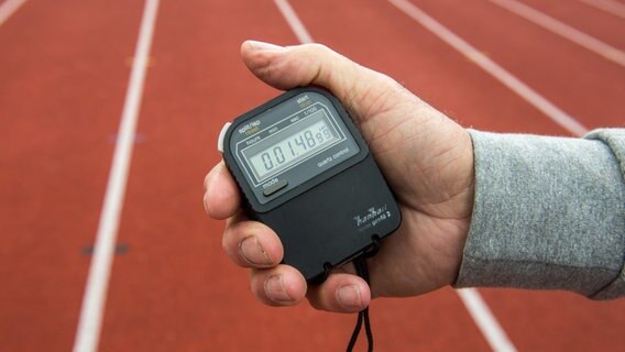 Eine Hand hält eine Stoppuhr vor eine Laufbahn. © dpa Foto: Armin Weigel