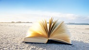 Ein aufgefächertes Buch im Sand am Strand. © fotolia.com Foto: by-studio