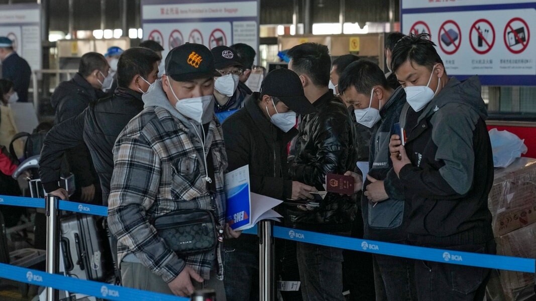 Reisende mit Mund-Nasen-Schutz überprüfen ihre Pässe, während sie am Schalter für internationale Flüge am Flughafen Peking anstehen. 