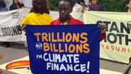 Eine Frau hält ein Transparent auf der Weltklimakonferenz COP29 in Baku, Aserbaidschan, darauf steht: Trillions not Billions for Climate Change. © Yasmin Appelhans / NDR Foto: Yasmin Appelhans