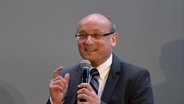 Der Politikwissenschaftler Prof. Emanuel Richter an der RWTH Aachen bei einer Podiumsdiskussion mit einem Mikrofon in der Hand. © Amerikahaus Köln 