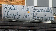 Auf einem Banner steht "Laßt die Familie Alviola in Hamburg". © Screenshot 