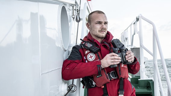 Ein Seenotretter mit einem Fernglas in der Hand schaut auf das Meer. © Kinescope/Achim Multhaupt 