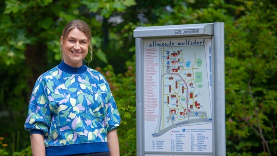 Pastorin Ina Jäckel steht vor einem Schild des Wohnprojekts Allmende Wulfsdorf. © Christine Raczka/Kirche im NDR 