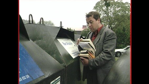 Ein Mann schmeißt Bücher in den Altpapiercontainer.  