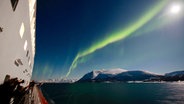 Vom Schiff aus fotografieren Reisende Polarlichter über einem Fjord. © NDR/Sebastian Sievert 