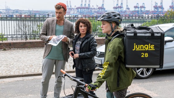 Nils Sanchez (Enrique Fiß, l.) und Harry Möller (Maria Ketikidou, M.) und Lieferdienstfahrerin Svea Perlmann (Henrike Fehrs, r.) stehen auf einer Straße. © ARD/Jörg Müller 