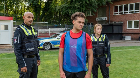 Ein Mitspieler kommt bewusstlos ins Krankenhaus, nachdem er aus der Trinkflasche von Matthias Kemper (Samy Abdel Fattah, M.) getrunken hat. Galt der Anschlag eigentlich ihm? Lukas Petersen (Patrick Abozen, l.) und Bente Hinrichs (Sinha Melina Gierke, r.) gehen dieser Frage nach. © ARD/Thorsten Jander 