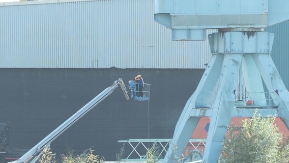 Ein Arbeiter auf einem Hubsteiger auf dem Sietas-Werftgelände in Neuenfelde, daneben ein Kran. © NonstopNews Foto: Screenshot