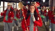 Eine Frau in einer roten Weihnachtstracht hält einen übergroßen Holzlöffel in der Hand. © NDR 